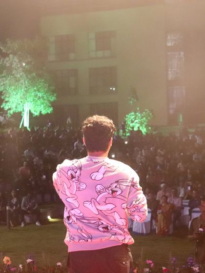 Comedian Aditya Kullu (Kullubaaazi) facing a large, seated outdoor audience at an alumni meet for IIM Visakhapatnam.
