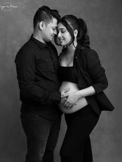 An intimate black and white maternity photo. The couple's hands gently cradle the baby bump, symbolizing their shared love and protection for their coming child.
