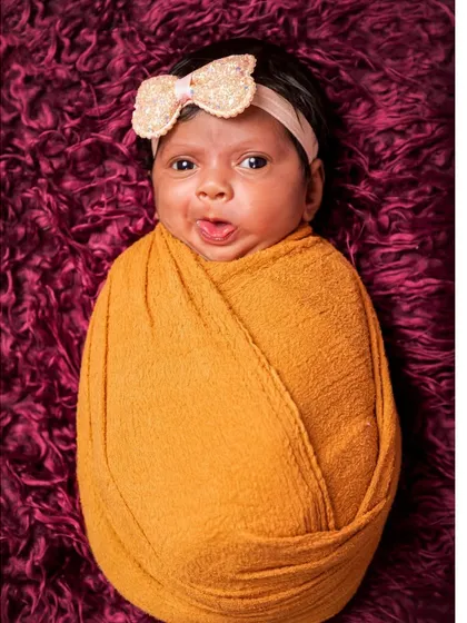 A simple and adorable portrait of a swaddled newborn with a funny expression. This shot captures the quirky and cute personality of a new baby against a rich, textured background.