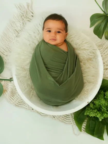 I love incorporating clean, modern themes into my newborn photography. This setup uses a simple white bowl, an olive green wrap, and fresh botanical leaves to create a striking and natural portrait of this beautiful, wide-eyed baby.