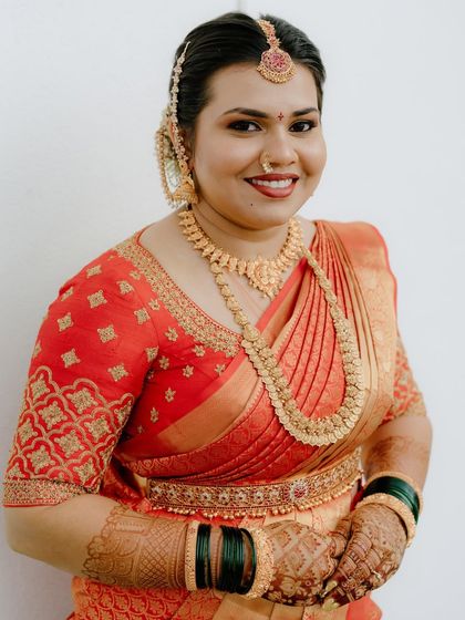 A close-up portrait of the bride, showcasing the detailed embroidery on her orange blouse and her traditional gold jewelry.
