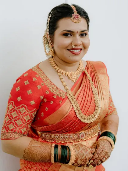 A close-up portrait of the bride, showcasing the detailed embroidery on her orange blouse and her traditional gold jewelry.