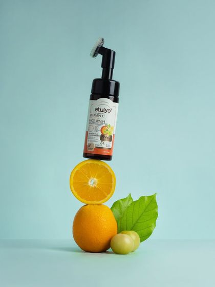A playful, gravity-defying shot of a Vitamin C face wash balanced on a stack of oranges. This creative concept is memorable and visually connects the product to its main ingredient.