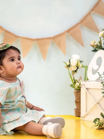 A classic first birthday portrait. The simple "one" sign and floral arrangement keep the focus on the baby's adorable expression.
