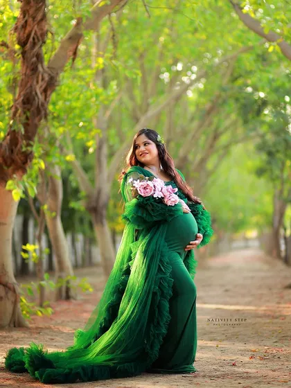 A lovely outdoor portrait with a pop of color from the pink flowers. The green gown and natural setting create a vibrant and fresh look.
