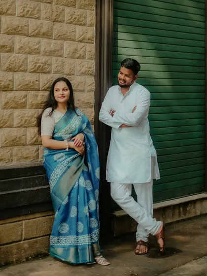 A candid moment between Abhishek and Saloni. Her in a beautiful blue saree and him in a classic white kurta, they share a look of love against a rustic wall.