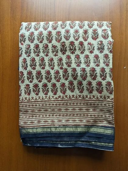 A closer look at a handblock print silk cotton saree. The traditional floral buti pattern in red and beige on a simple off-white base is classic and elegant.