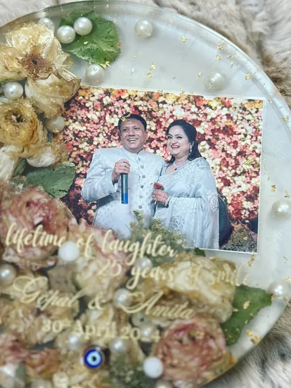 This circular resin art piece was created to celebrate a silver anniversary. The preserved flowers, pearls, and a cherished photo make it a truly personal and heartfelt gift.