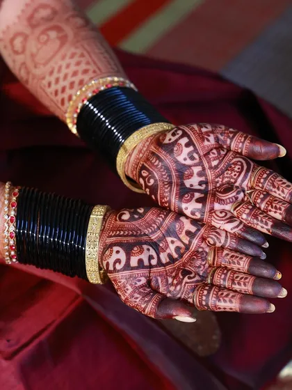 A close-up of a rich, dark henna stain on the palms, paired with traditional black bangles. The contrast makes the elephant designs stand out beautifully.