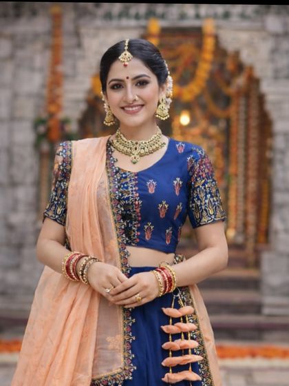 A smiling close-up portrait in the blue silk lehenga, showing the detailed blouse embroidery and the beautiful gold jewellery set.