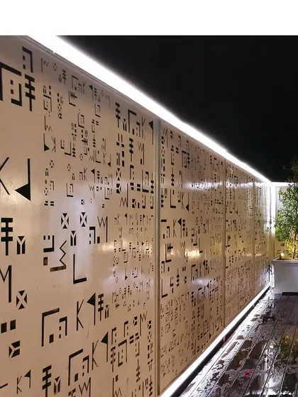 A close-up of the custom perforated screen on the facade of a modern home. The play of light through the abstract patterns creates a unique and dynamic effect, especially at night.