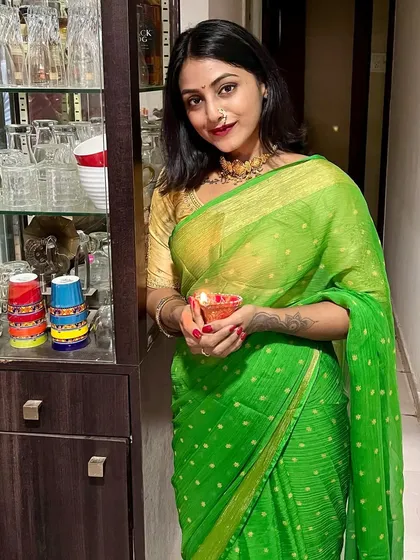 Holding a diya during Diwali. The simple elegance of this green saree makes it a perfect choice for celebrating the festival of lights at home.