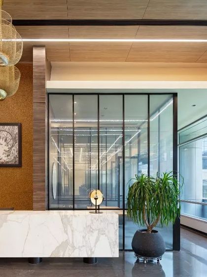 The reception lobby for the APT office in New Delhi. A clean, white marble desk is set against a backdrop of warm wood and glass, creating a look of upscale, modern professionalism.