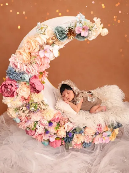 A wide shot of a newborn sleeping on a floral crescent moon prop. This view showcases the full scale and artistry of the elaborate, custom-designed setup.