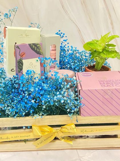 A rustic wooden crate filled with blue gypsophila, a potted plant, and other pampering gifts. This was another one of our special hampers for Mother's Day.
