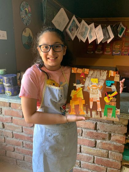 A smiling student holds up her completed "Three Musicians" collage, a wonderful tribute to Picasso's cubist masterpiece.