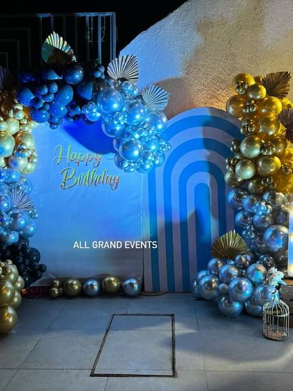 The full view of the blue and gold birthday stage, complete with marquee initials, a birdcage prop, and spotlights to highlight the decor.