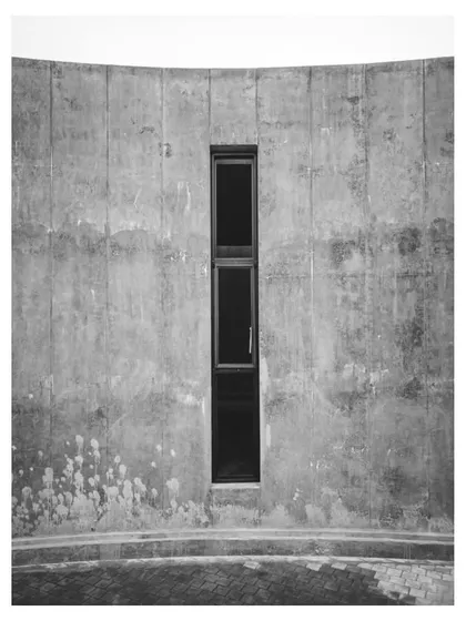A black and white photo of a narrow window in the concrete wall, emphasizing its form and the texture of the surface.