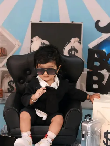This boss baby is the epitome of cool, adjusting his sunglasses while sitting in his chair, surrounded by bags of money.