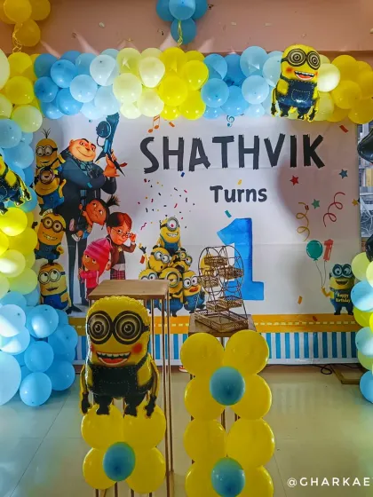 A fun-filled Minions-themed first birthday. The setup includes a large backdrop with Gru and the Minions, a yellow and blue balloon arch, and Minion foil balloons.