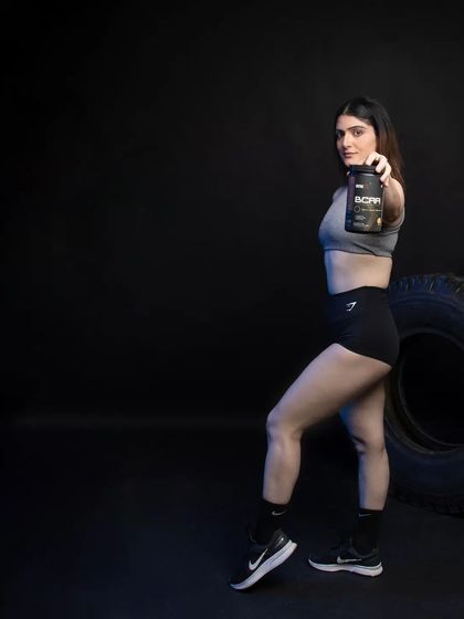 A full-body shot where the model holds the BCAA product out towards the viewer. The dark, atmospheric background ensures the product and the model are the sole focus, ideal for impactful social media posts.