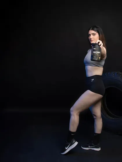 A full-body shot where the model holds the BCAA product out towards the viewer. The dark, atmospheric background ensures the product and the model are the sole focus, ideal for impactful social media posts.