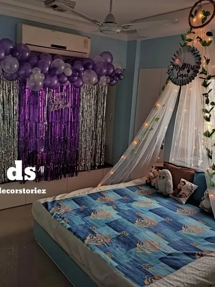 A full view of a bedroom decorated for a special occasion. We combined a purple and silver balloon backdrop with a beautiful fairy light canopy over the bed, creating a cozy and celebratory space.