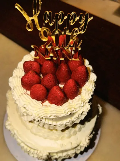 A two-tiered winter favorite, topped with fresh strawberries and a custom 'Happy 90th Nani' topper. It’s an honor to be part of such milestone celebrations.