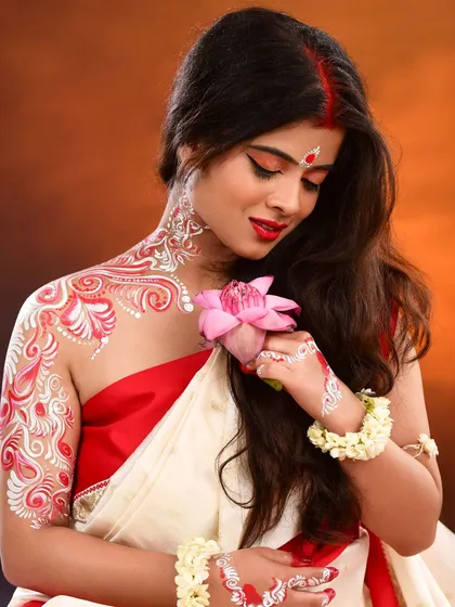 A creative and traditional Bengali look for a themed photoshoot. This features classic eye makeup with a red bindi, paired with intricate white and red Alpona body art on the neck, shoulder, and arm, demonstrating my skill in artistic and cultural makeup.