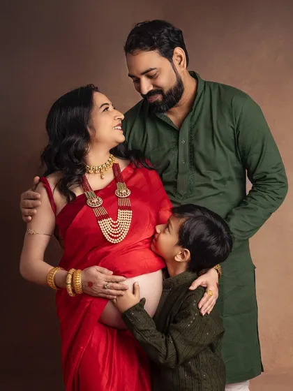 A moment of quiet connection before the family grows. I love how the traditional red saree and jewelry add such elegance to this maternity portrait, while her son's gentle kiss on the baby bump tells a story of love and anticipation.