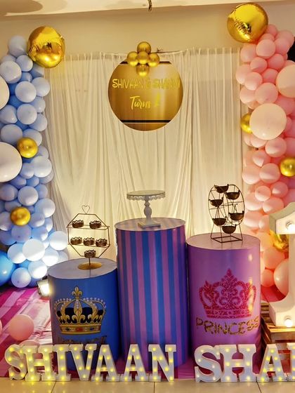 A "Prince & Princess" themed first birthday for twins. The setup features a blue and pink color scheme, crown-themed plinths, and a large light-up number '1'.