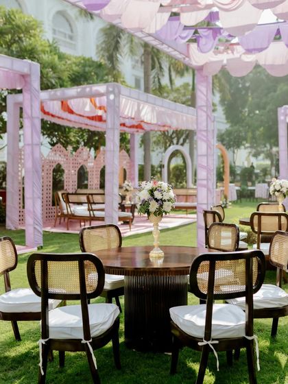 A charming table setup at the garden Mehendi, featuring dark wood and cane chairs that provide a beautiful contrast to the soft pastel decor.