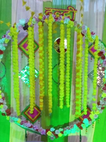 A close-up of a Haldi backdrop with a marigold ring against green and yellow drapes. The "Haldi" sign is made from flowers, adding a beautiful, handcrafted detail.