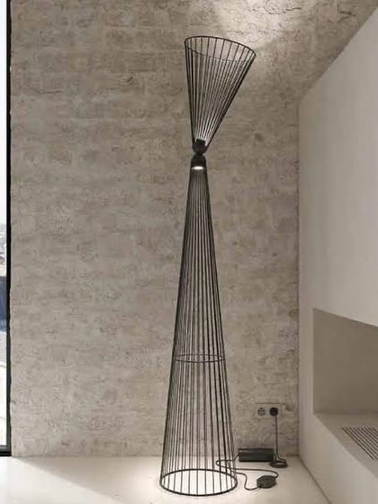 The Ikonika floor lamp against a textured concrete wall, its clean, geometric lines creating a striking contrast with the raw material of the wall.