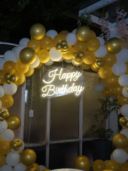A close-up of a "Happy Birthday" neon sign surrounded by a gold and white balloon arch. We capture the festive details of your event.