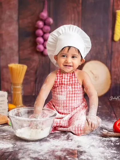 A full view of our little chef's kitchen. The personalized chalkboard, fresh veggies, and wooden backdrop create an authentic and playful setting. It's the perfect recipe for an unforgettable first birthday shoot.