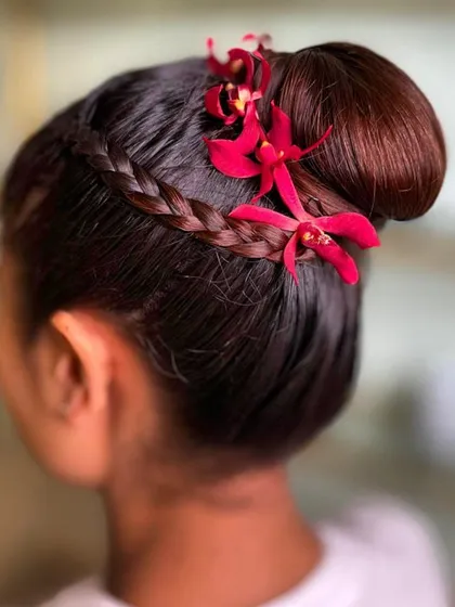 A radiant addition to our spring styles collection. This sleek braided bun is accented with vibrant red orchids, capturing the essence of spring's beauty.