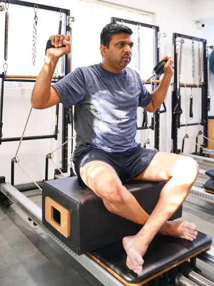 A seated arm exercise on the reformer box allows this client to focus on building upper body strength and shoulder stability. Pilates provides a challenging workout for men seeking functional fitness.