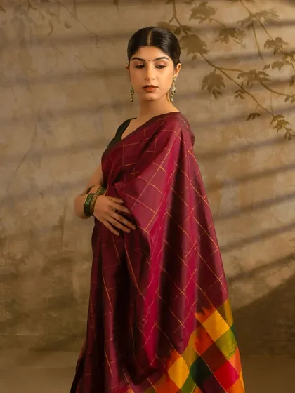 A close-up shot of a model wearing a Kumaran Silks saree, focusing on the drape and fabric. The soft, painterly background adds to the image's elegance.