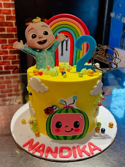 A sunny yellow Cocomelon cake for Nandika's second birthday, topped with a happy JJ and a bright rainbow.