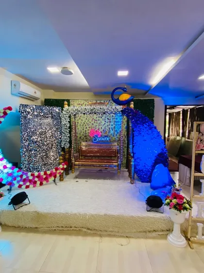 An elegant baby shower stage with a silver sequin backdrop, a traditional swing, and a stunning peacock figure made of blue flowers.