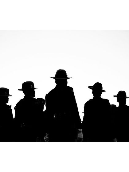 A powerful black and white silhouette of a group of soldiers in wide-brimmed hats. The high-contrast composition creates a graphic and iconic image of unity and discipline.