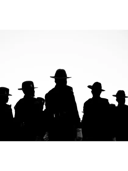 A powerful black and white silhouette of a group of soldiers in wide-brimmed hats. The high-contrast composition creates a graphic and iconic image of unity and discipline.