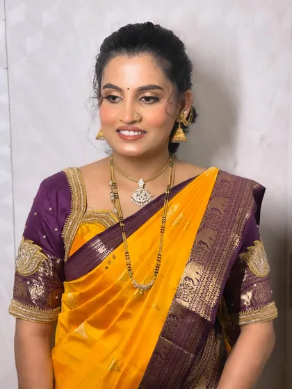 A classic and elegant look for a son's naming ceremony. The makeup is kept fresh and bright to complement the vibrant yellow and purple Kanjeevaram saree, ensuring she looks her absolute best for the family photos.