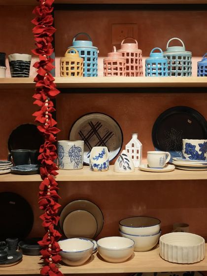 A view of our studio shelves, beautifully stocked with a colorful array of finished handmade pottery. You can see lanterns, plates, bowls, and mugs, showcasing the breadth of our work.