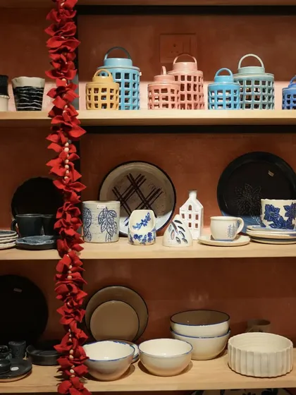 A view of our studio shelves, beautifully stocked with a colorful array of finished handmade pottery. You can see lanterns, plates, bowls, and mugs, showcasing the breadth of our work.