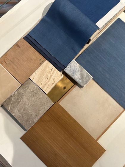 A material palette combining rich blue fabric with various wood tones, marble samples, and a touch of brass. This mood board captures the intended balance of color, texture, and warmth for a sophisticated office interior.