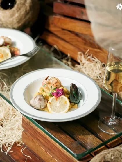A stunning seafood dish with mussels and prawns served over a bed of risotto, garnished with a lemon wheel. The composition and colours make this a true centrepiece of a plated dinner.