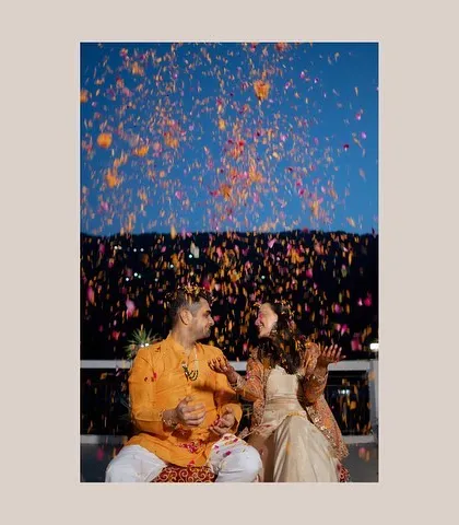 A shower of flower petals over the couple during their Haldi ceremony. The vibrant colors against the blue sky create a stunning and joyful image.