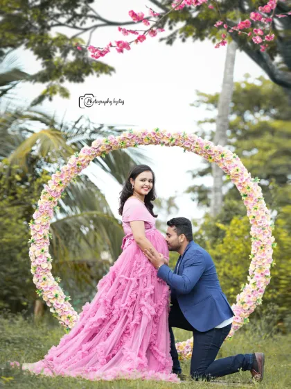 A sweet couple's portrait in front of a circular floral prop. The father-to-be kisses the baby bump, creating a heartwarming memory.